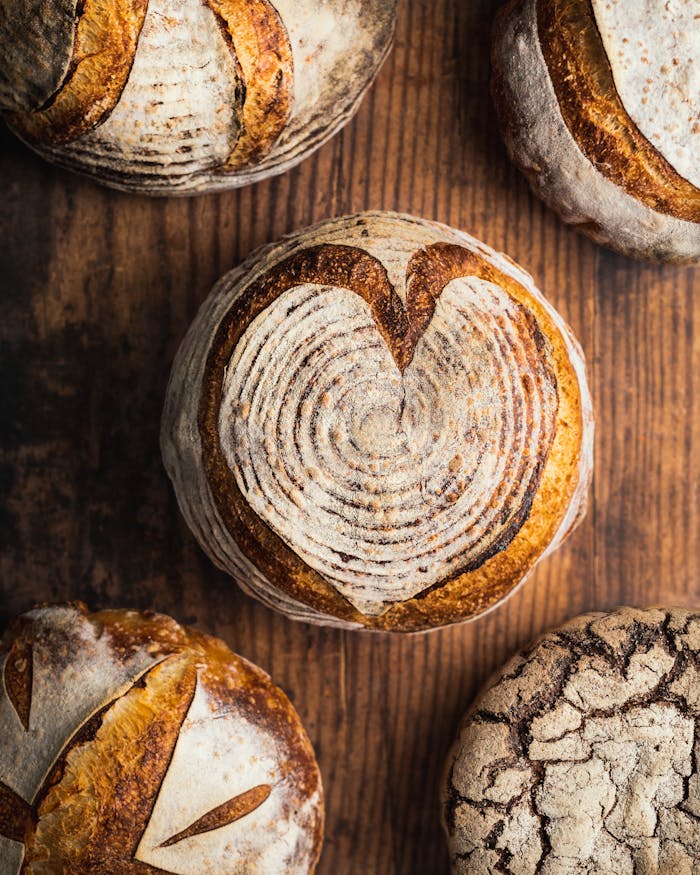 assorted-artisan-bread-loaves-on-wooden-table-28673749 Top view of various artisan bread loaves with intricate designs, perfect for bakery promotions.