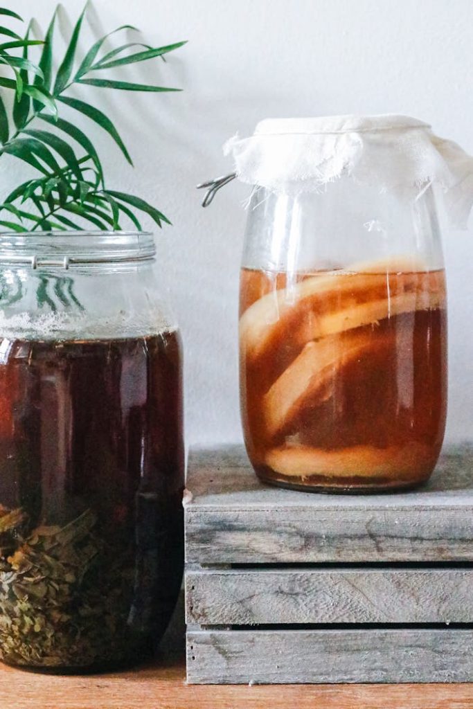 jars-with-kombucha-and-dark-herbal-beverage-6605199 Close-up of kombucha brewing in jars with a rustic setting, showcasing natural fermentation process.